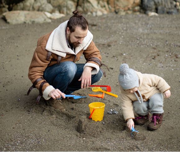 A person and a child playing with sandDescription automatically generated with low confidence